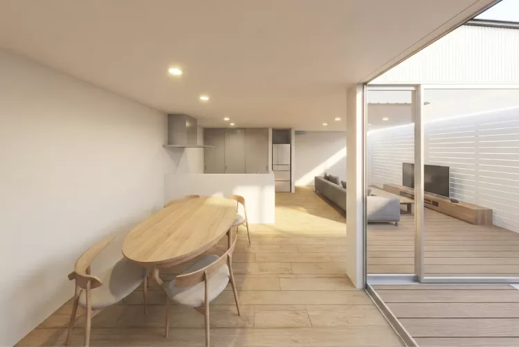 ナラ材のダイニングテーブル越しに見る、モルタル風のキッチンとリビング。光が溢れる明るいLDKの全景。